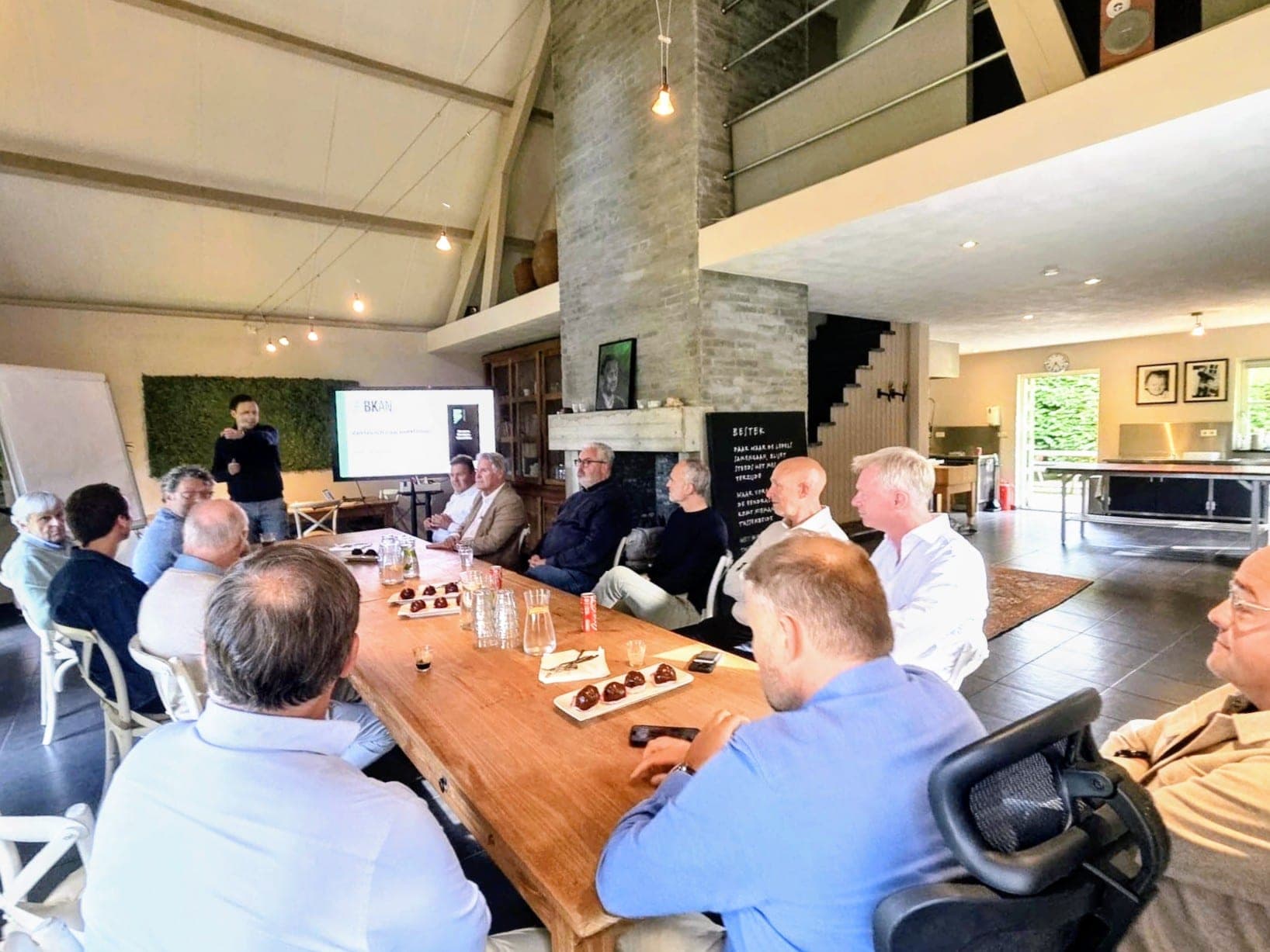Een groep volgt een presentatie aan de lange tafel